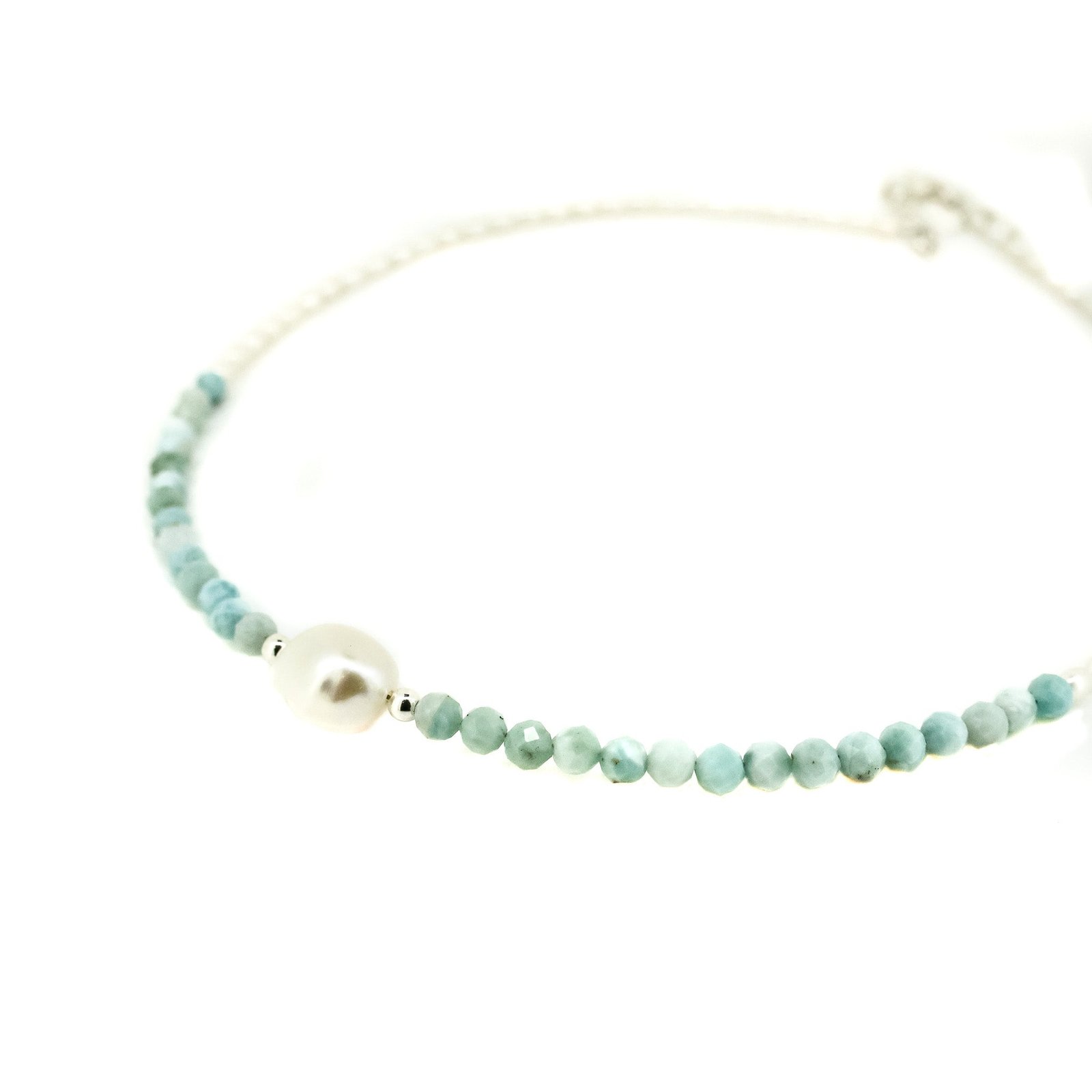 A necklace with blue larimar gemstones and a white keshi pearl, with small blue and white pearls strung along a fine chain.